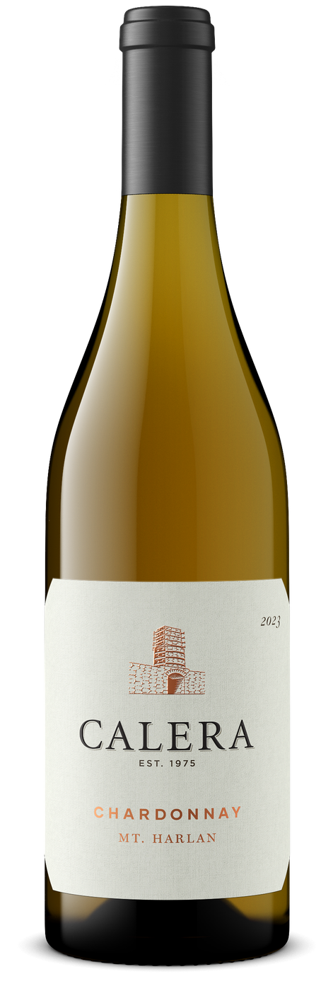 Genom glaset syns ett gyllene vin, och flaskan har svart kapsel och en ljus etikett med en koppartryckt kalkugn av sten samt texten Calera, Est. 1975, Chardonnay, Mt. Harlan och årtalet 2023. Calera Mt Harlan Chardonnay, flaska. Genom glaset syns ett gyllene vin, och flaskan har svart kapsel och en ljus etikett med en koppartryckt kalkugn av sten samt texten Calera, Est. 1975, Chardonnay, Mt. Harlan och årtalet 2023.